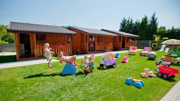 Una cabaña de madera con un porche y un patio cubierto de césped, con juegos infantiles.