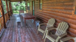 A wooden cabin with a porch, a table, and two Adirondack chairs. - LUXURY LOG CABIN #1 ON THE FRIO RIVER (Leakey)