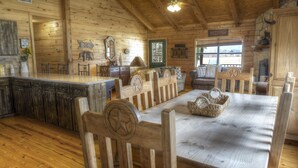 Een rustiek houten interieur met een eettafel, stoelen, een keukenhoek en een gezellige zithoek met een bank en fauteuils.