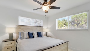 A bedroom with a bed, two bedside tables, a ceiling fan, and a window with blinds.