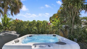 A hot tub in a garden with lush greenery and a clear blue sky.