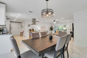 Una cocina moderna con armarios blancos, un comedor con mesa y sillas de madera, y un ventilador de techo.