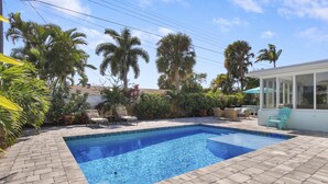 A rectangular swimming pool with a tiled edge, surrounded by a brick patio.