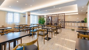 Un'ampia sala da pranzo con numerosi tavoli e sedie, una cucina sullo sfondo e un pannello decorativo con motivi geometrici.