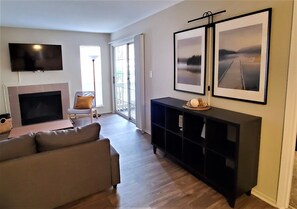 A living room with a fireplace, a sofa, a TV, and a bookshelf with framed pictures.