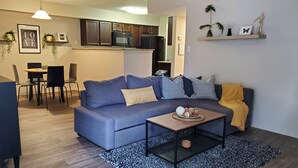 Un salon moderne avec un canapé bleu, une table basse et un coin repas avec des chaises.