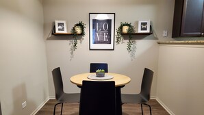 Un coin repas avec une table ronde, des chaises noires et une petite plante posée sur la table. Deux tableaux encadrés sont accrochés au mur, au-dessus de la table.