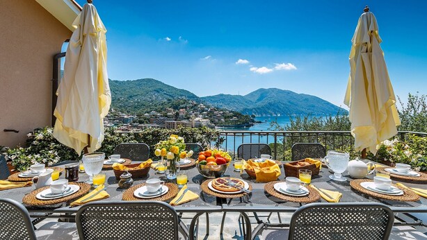 A table set for breakfast with a scenic view of a coastal town and mountains. - Villa Baia Blu 12, Emma Villas (Recco)