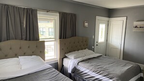 A bedroom with two beds, a window with curtains, a door, and a small shelf with items.