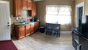 A kitchen with wooden cabinets, a granite countertop, a black refrigerator, and a window with curtains.