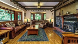 A cozy living room with a fireplace, wooden furniture, and large windows.