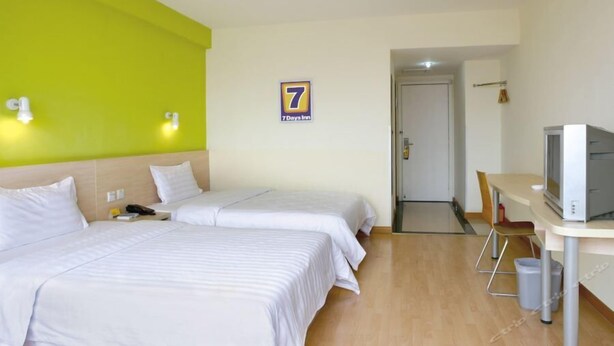 Ein Hotelzimmer mit zwei Betten, einem Schreibtisch mit Fernseher und einer Tür zu einem anderen Raum.