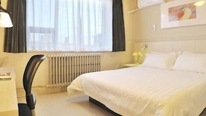 A hotel room with a bed, a chair, a radiator, a window with curtains, a wall-mounted air conditioner, and a small table with a vase of flowers. - Jinjiang Inn Hohhot Erdos East Street Branch (Hohhot)