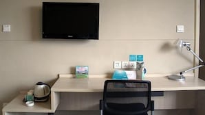 A hotel room with a flat-screen TV mounted on the wall, a desk with a laptop, a kettle, and a coffee maker. There is a chair in front of the desk, and a desk lamp is on the desk. - Jinjiang Inn Hohhot Erdos East Street Branch (Hohhot)