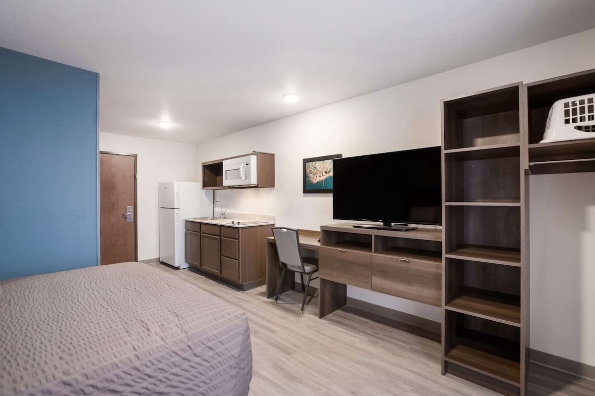 A compact room with a bed, kitchenette, desk, and TV.