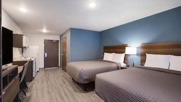 Een hotelkamer met twee bedden, een bureau en een kitchenette.