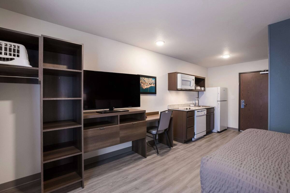 A compact room with a bed, a desk with a chair, a television, a microwave, a refrigerator, and a wardrobe.