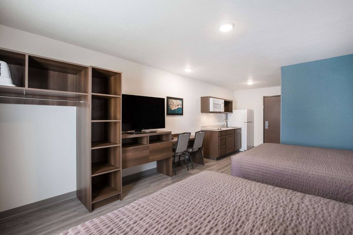 A hotel room with a bed, a desk with a chair, a television, a microwave, and a wardrobe.