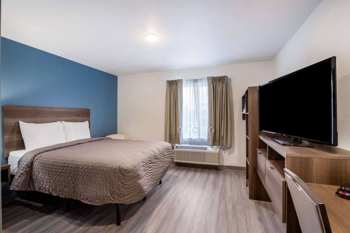 A hotel room with a bed, a TV, a desk, and a window with curtains.