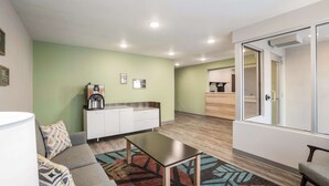A modern living room with a sofa, coffee table, and a kitchenette area with a coffee machine. - WoodSpring Suites Detroit Madison Heights (Madison Heights)
