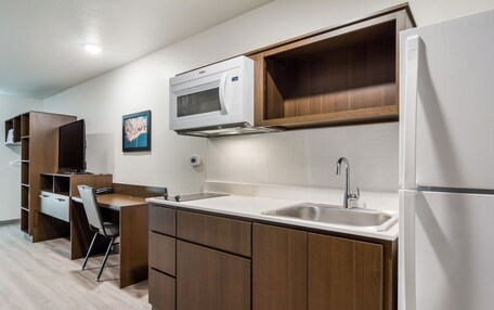 A compact kitchen with wooden cabinets, a microwave, a sink, and a refrigerator.