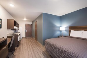 A hotel room with a bed, desk, kitchenette, and a door leading to another room. - WoodSpring Suites Detroit Madison Heights (Madison Heights)