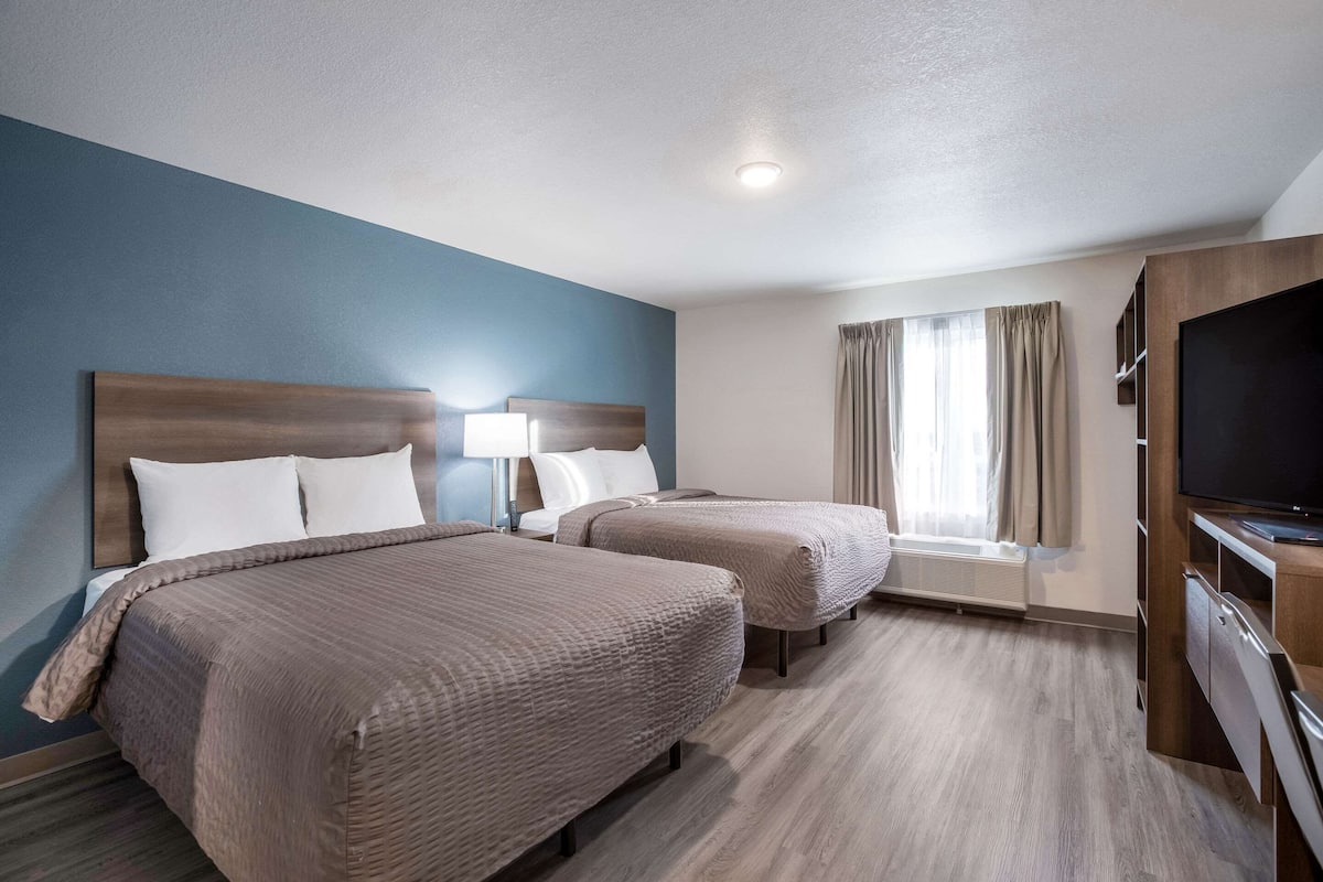 A hotel room with two beds, a television, and a window with curtains.