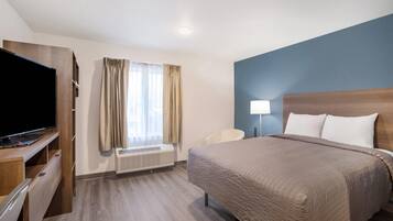 A hotel room with a bed, a TV, a desk, a chair, a lamp, and a window with curtains.