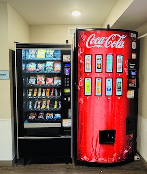 Two vending machines, one with snacks and the other with beverages including Coca-Cola. - WoodSpring Suites Detroit Madison Heights (Madison Heights)