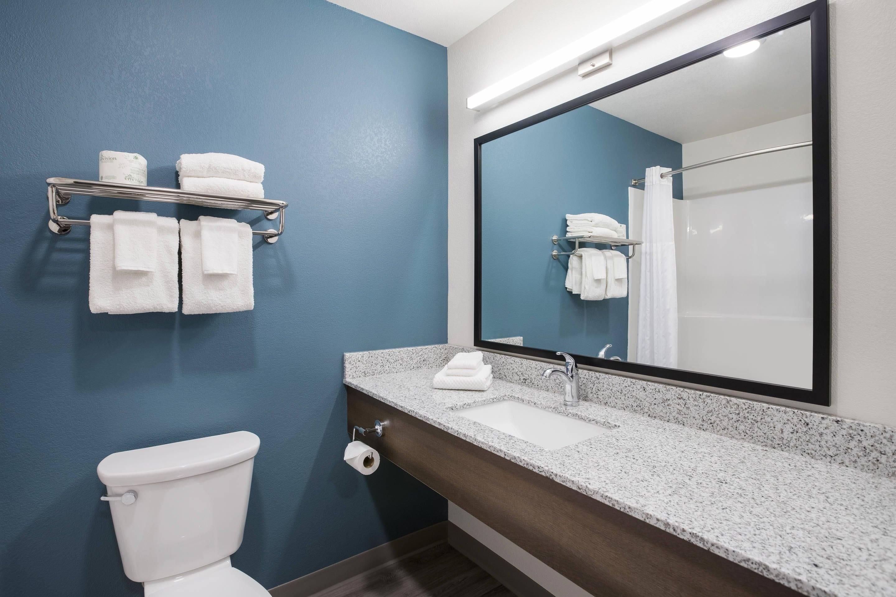 A bathroom with a toilet, a sink, a mirror, and a towel rack with folded towels.