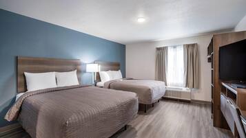 A hotel room with two beds, a TV, and a window with curtains.