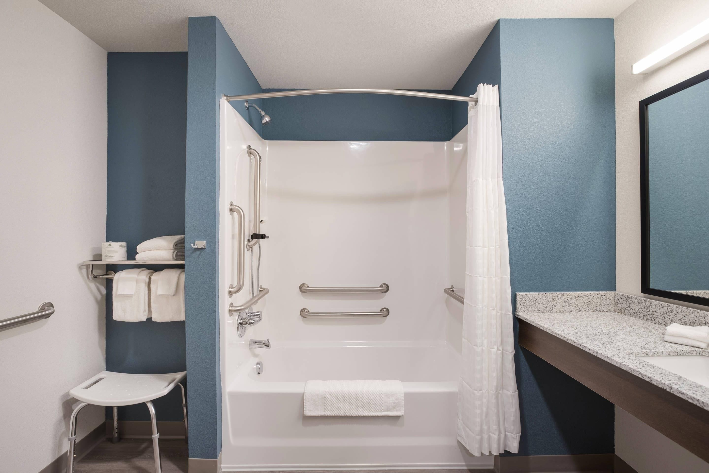A modern bathroom with a walk-in shower, grab bars, a white towel, and a vanity with a mirror.