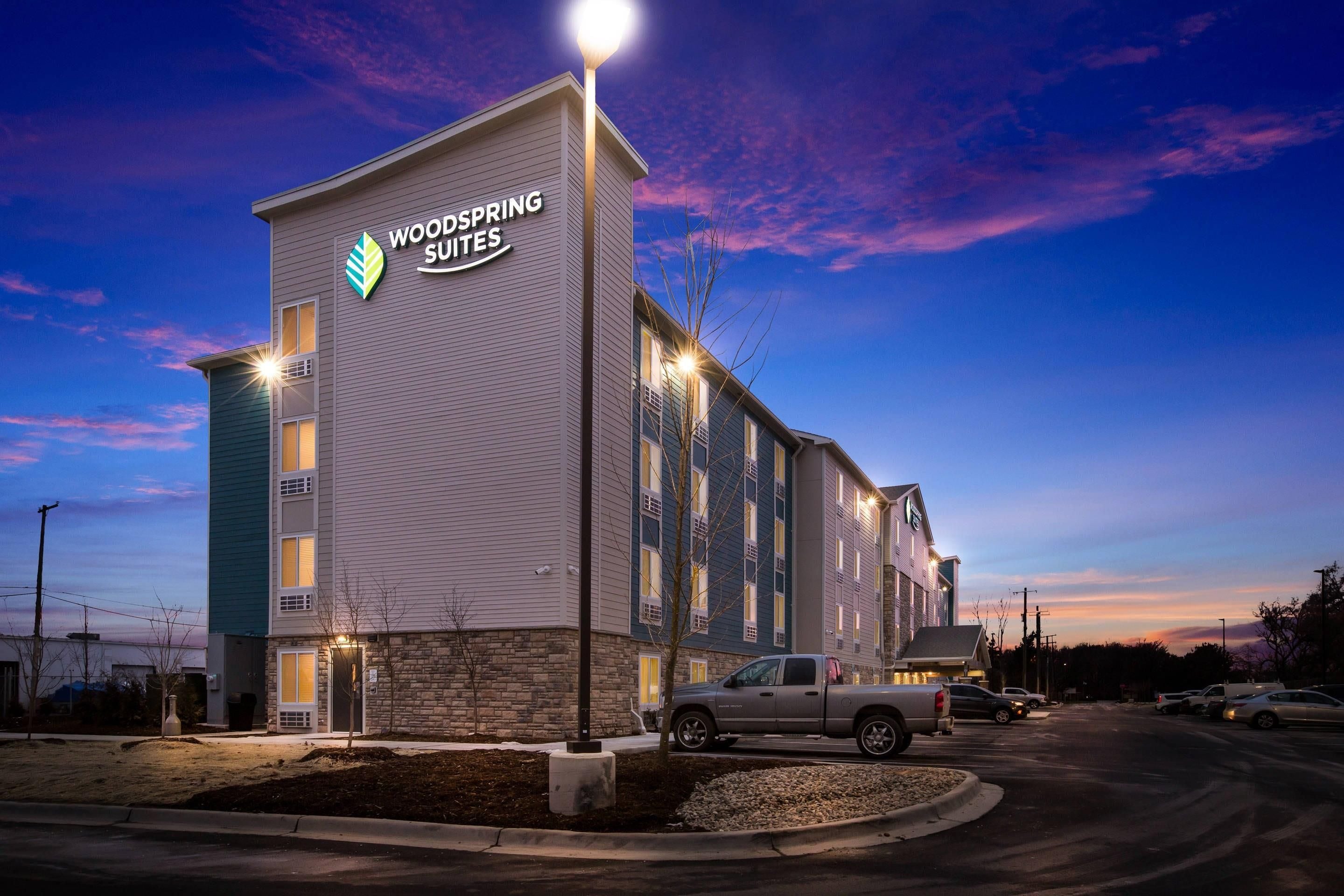 Un bâtiment d'hôtel avec une enseigne indiquant « WOODSPRING SUITES » et un parking avec des véhicules.