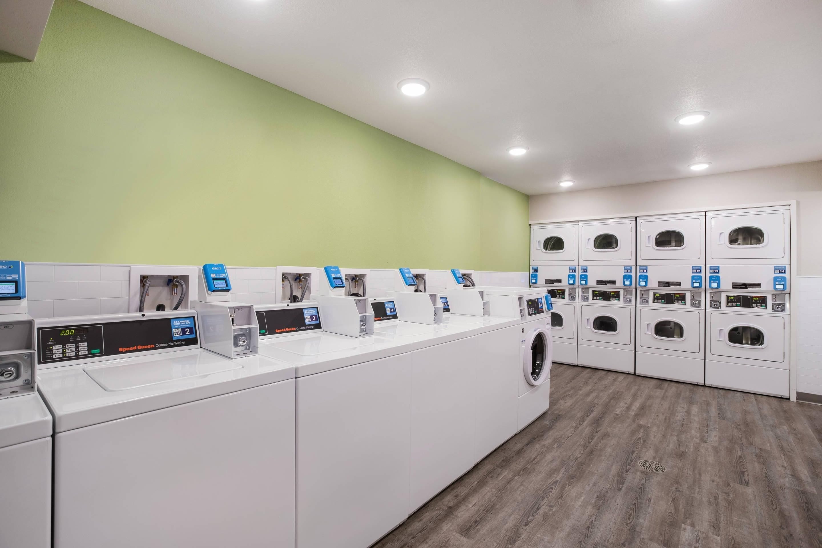 A laundry facility with multiple washing machines and dryers, each with a control panel.