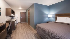 A hotel room with a bed, bedside table, lamp, and a kitchenette area with a sink and cabinets. - WoodSpring Suites Detroit Madison Heights (Madison Heights)