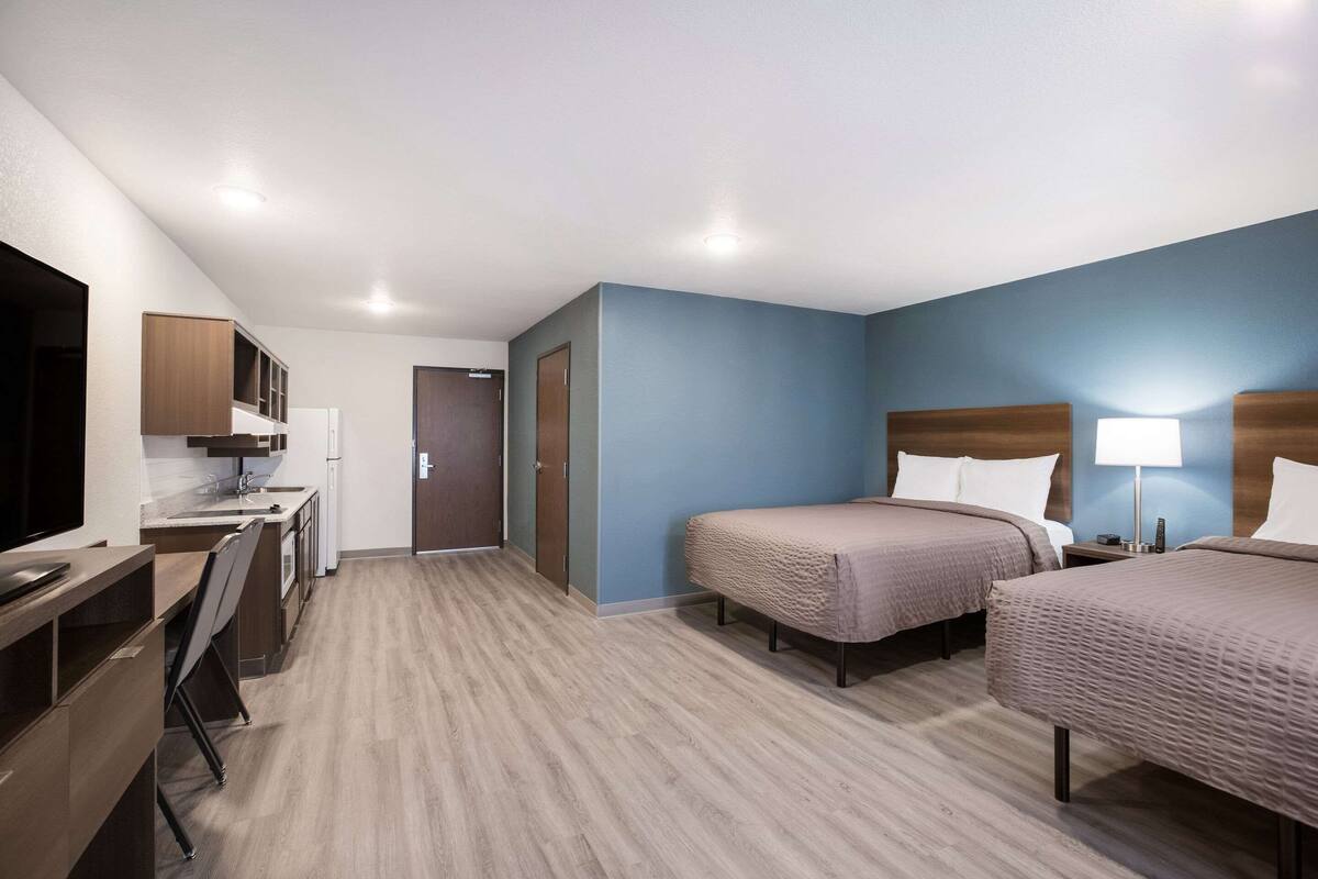 A hotel room with two beds, a desk, a TV, and a kitchenette.