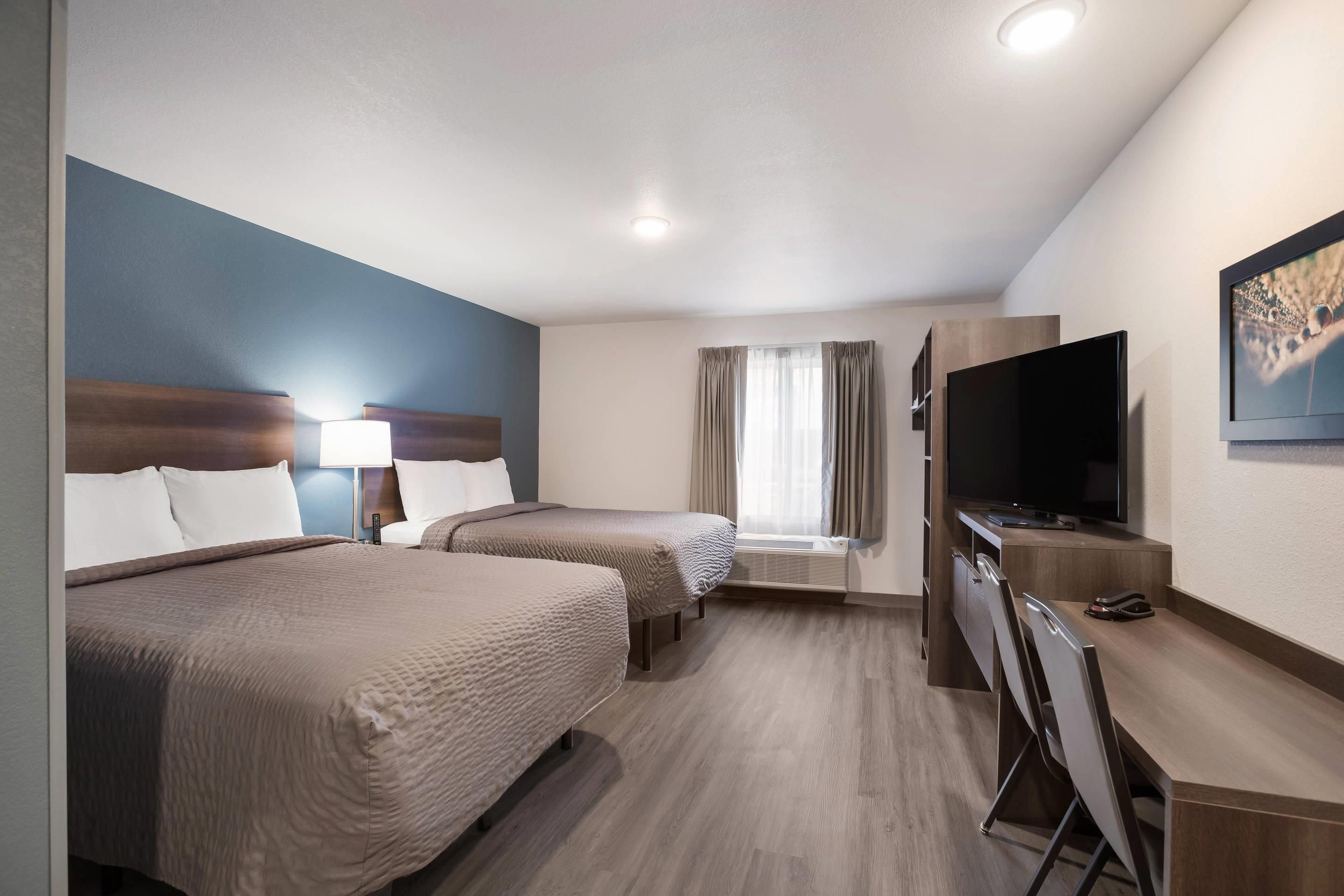 A hotel room with two beds, a TV, a desk, and a window with curtains.