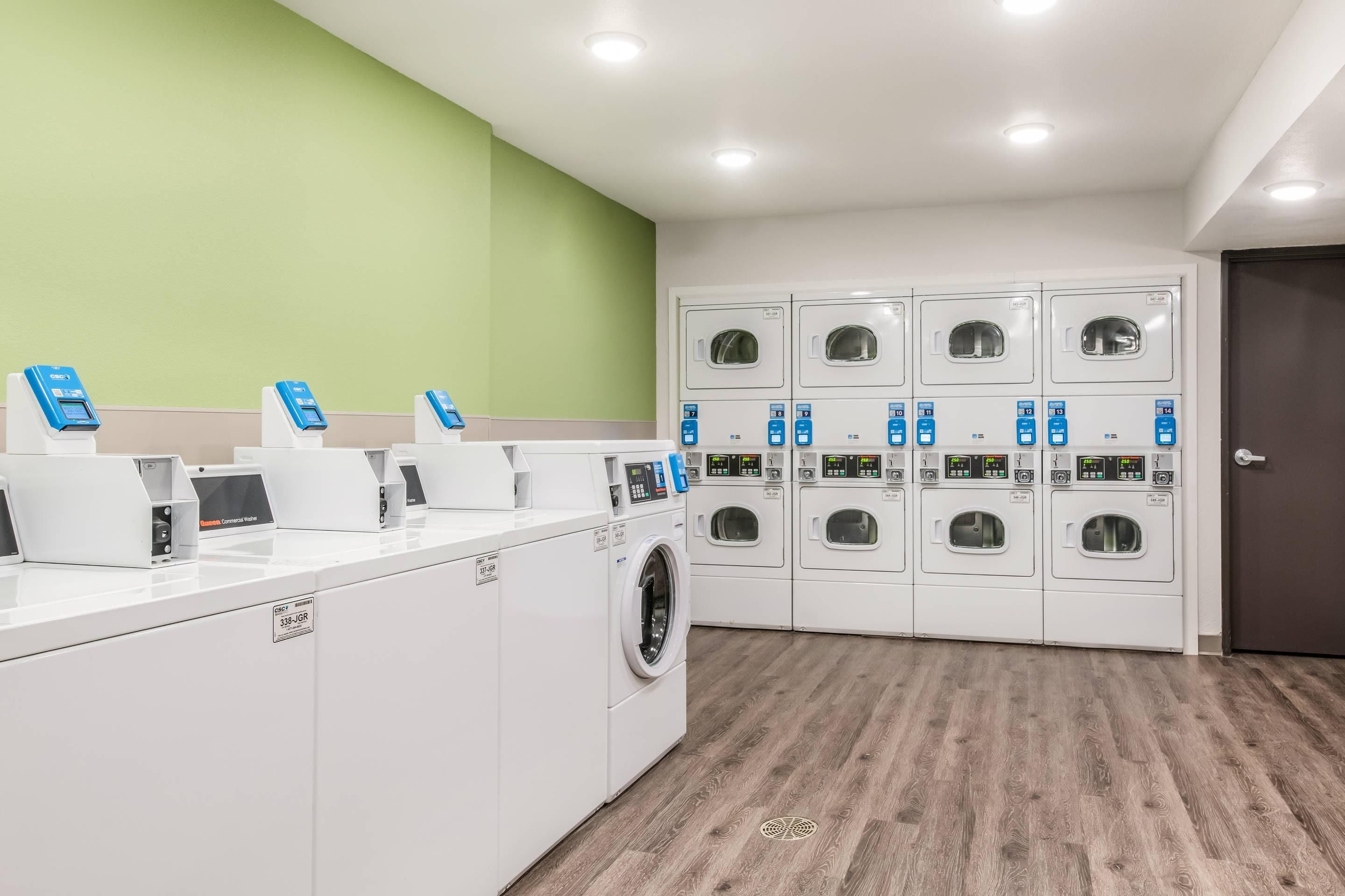 A laundry facility with multiple washing machines and dryers, a payment station, and a green wall.