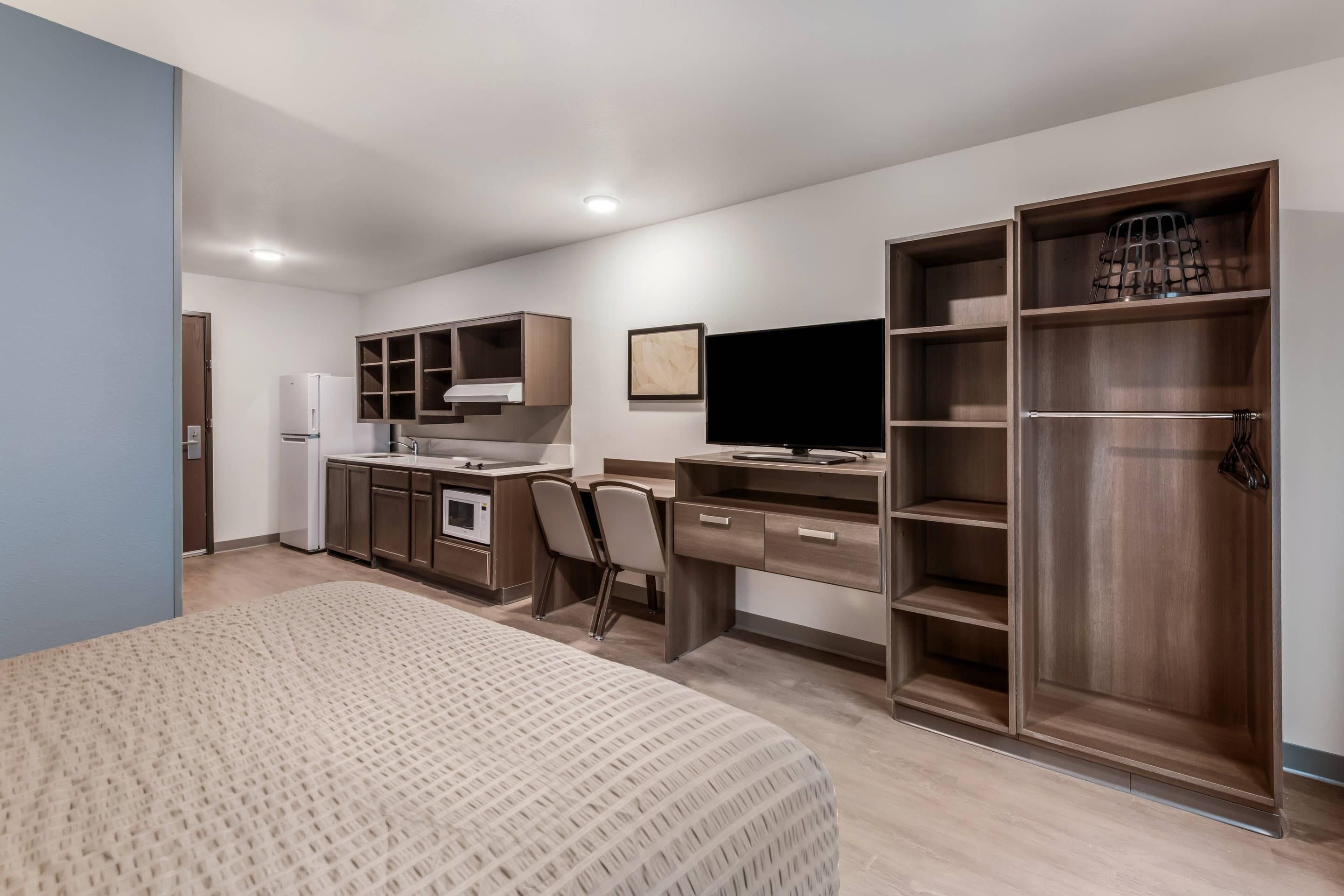 Habitación de hotel compacta con kitchenette, una cama, un escritorio con silla, televisión y armario.