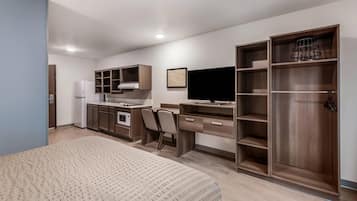 Habitación de hotel compacta con kitchenette, una cama, un escritorio con silla, televisión y armario.