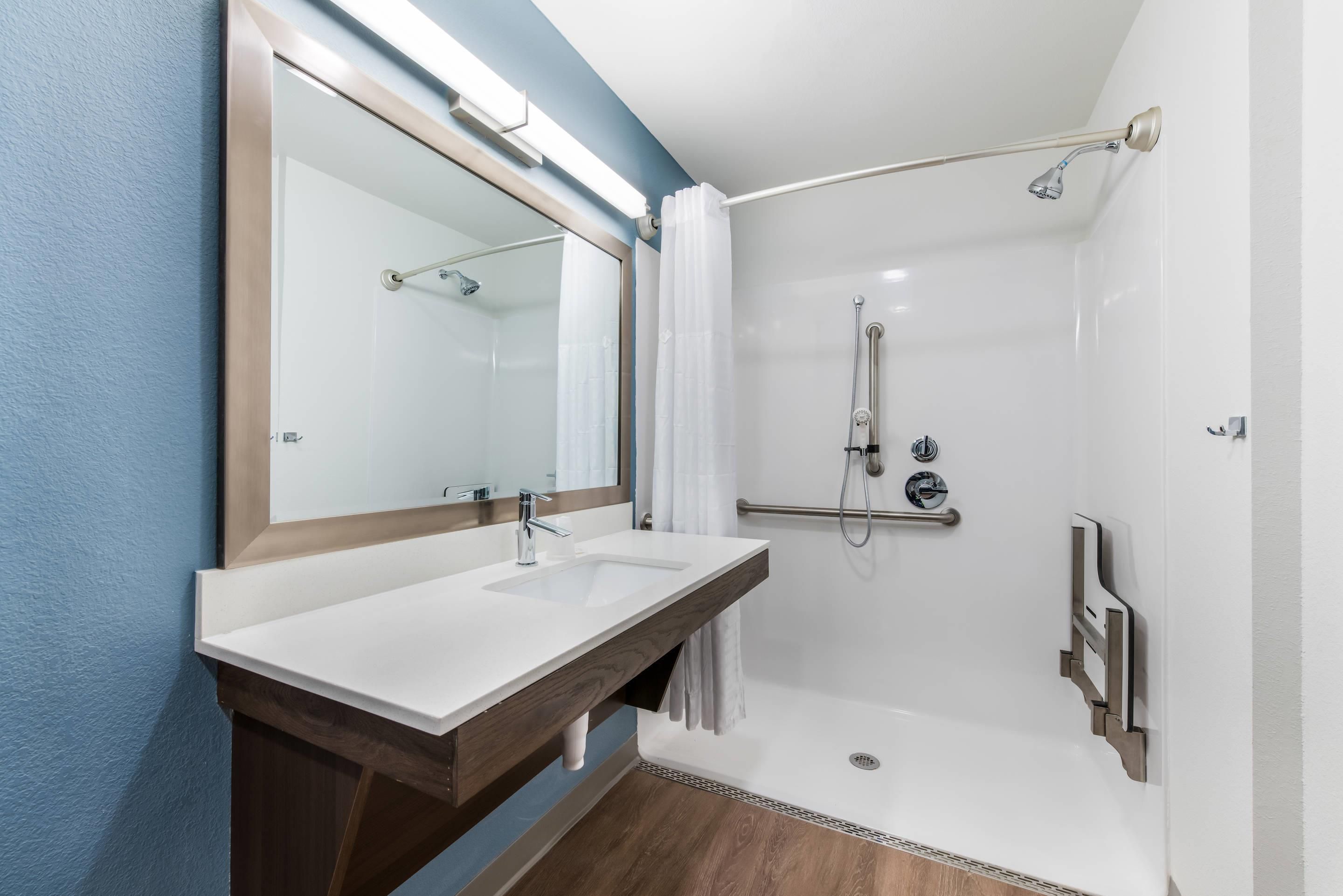 A modern bathroom with a double sink, a shower with a handheld showerhead, and a large mirror.