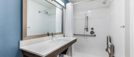 A modern bathroom with a double sink, a shower with a handheld showerhead, and a large mirror.