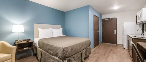 Ein Hotelzimmer mit Bett, Nachttisch, Lampe, Stuhl und einer Küchenzeile.
