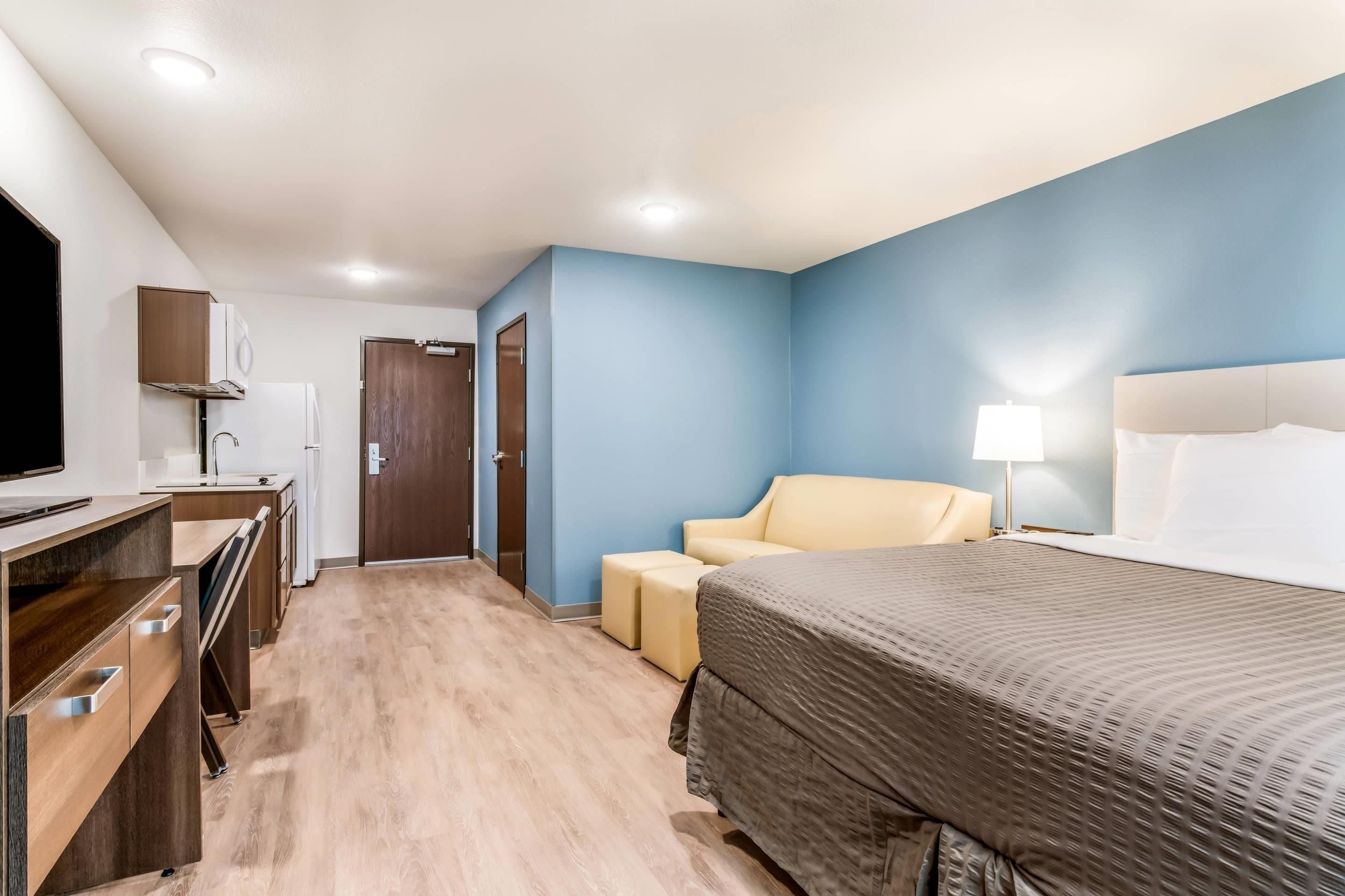 A hotel room with a bed, a desk with a computer, a chair, a TV, and a door.