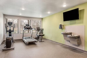 Un gimnasio con cintas de correr, una bicicleta estática y un televisor montado en la pared.