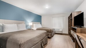 Habitación de hotel con dos camas, televisión, escritorio y ventana con persianas.