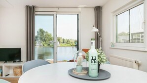 A modern room with a large window, a flat-screen TV, a dining table with a bottle of Merlot, and a lamp. - Picturesque holiday home with garden on open waters (Terherne)
