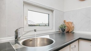A kitchen with a stainless steel sink, a window above the sink, and a clock on the wall. - Picturesque holiday home with garden on open waters (Terherne)
