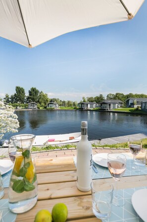 Une table au bord du lac, avec une bouteille, des verres et un vase de fleurs.