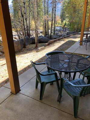 Une terrasse extérieure avec une table ronde et quatre chaises, entourée d’arbres et d’un mur de pierre.